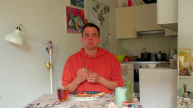 Bir adam, parlak bir mutfak masasında rahatça oturur, lezzetli bir kahvaltı ve ferahlatıcı bir içeceğin tadını çıkartır, nişanını ve dikkatini çeken birçok açıdan görüntülenir.