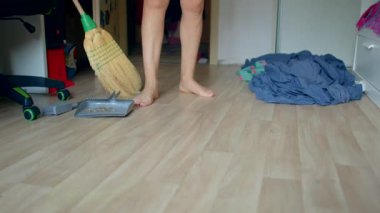 Sıradan giyinmiş bir birey aktif olarak odalarını temizliyor, yerleri süpürüyor ve dağınık giysileri yönetiyor, yaşam alanlarını düzenleyip düzenliyor.