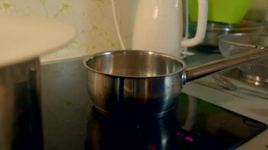 Bu videoda, indüksiyon sobasında yemek pişiren, tencereye su döken, kürdanla karıştıran, ev yemeklerini basitleştiren bir kişi görülüyor.