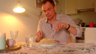 Adam akşam yemeğinin keyfini çıkarıyor, adam yemek masasında makarna çeviriyor, beyaz adam mutfak ışıklarının altında makarnanın tadını çıkarıyor, adam akşamları mutfak masasında rahat yemeğin tadını çıkarıyor.