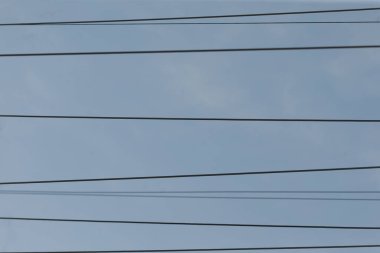 Karışık kentsel güç kablolarının minimalist sahnesi, birbirine dolanmış elektrik hatları mavi gökyüzüne karşı ufuk çizgisine uzanır, parlak şehir mavi gökyüzünün altında çapraz elektrik kabloları ve direklerin görüntüsü