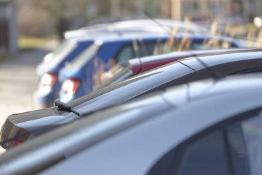 Park halindeki araçlar sığ odaklı sıkışık kompozisyonda dizilmiş araçların çatılarını ve arka kısımlarını gösteriyor. Bokeh röfleleri, metalik yansımaları ve sabah ışığı hareketsiz kentsel dönüşüm havası yaratıyor.