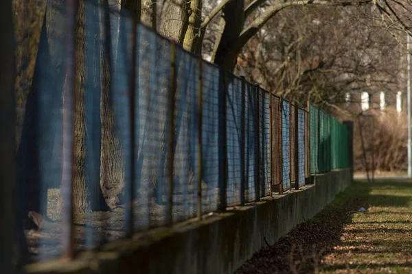 Güneşli yol sahnesi, desenli çitleri olan koşucu silueti, paslı metal paneller ve gölgeler içeren sessiz mahalle, mevsimlik çıplak ağaçlar, güneşli gezinti güvertesi boyunca desenli gölgeler