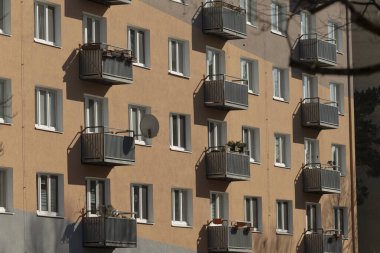 Sıcak cephede güneşli apartman balkonları uydu anteni, metal korkuluklar, sıva dokusu, tekrarlayan pencereler ve hoş şehir atmosferi yaratan ince gölgeler olan çok katlı evler.
