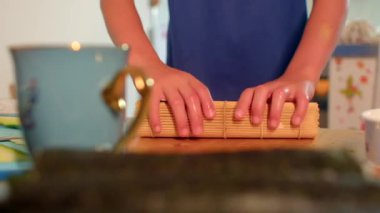 Evde bambu hasırında suşi hazırlamak, kadın ustalıkla suşiyi pirinçle sarmak ve mutfakta deniz yosunu.