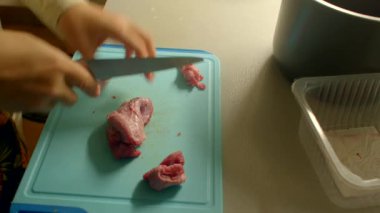 Güvertede çiğ domuz eti dilimleyen eller, sıcak mutfak ışığı, ev aşçısına yakın çekim, keskin bıçaklı filetoları hazırlamak, yanında plastik kap, hijyenik yüzey ve akşam yemeği için ölçülü porsiyonlar.
