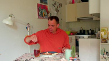  Kırmızı kapüşonlu adam mutfak masasında sessizce yemek yiyor. Kırmızı kapüşonlu adam sessizce yemeğini yiyor.