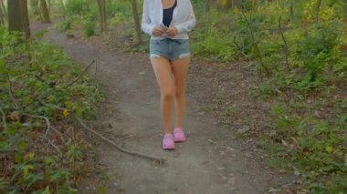 Doğadaki kadın, gün batımında canlı giyinmiş ve sakin bir şekilde orman yolunda yürüyor.