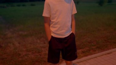 Beyaz genç dans ediyor ve akşam karanlığında parkın kenarında yürüyor, anlamlı kollar, kasvetli şehir ışıkları, sinematik titreşim