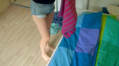 Kadın yatağı düzenler, yatağın üzerine pembe battaniye serer, kadın pürüzsüzlüğü serer, yatağa pembe çizgili battaniye serer, kadın telaş yapar ve yatağın üzerine düzgün pembe çizgili battaniye serer.