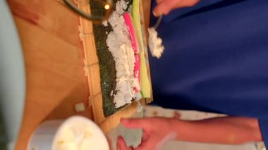Suşi pilavını kaşık ile yosun paspasına dökmek, rengarenk dolgu maddeleri ve pirinci nori 'nin üzerine titizlikle dökmek, el düzenlemeleri.