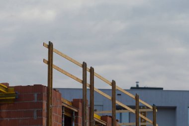 Taze tuğla duvar ve bulutlu gökyüzü altında ahşap iskeleye sahip inşaat alanı, hammaddeler ve artan çerçeve işaretleme gelişimi ve gelecekteki ev inşaatı, müteahhit veya mimar için ideal