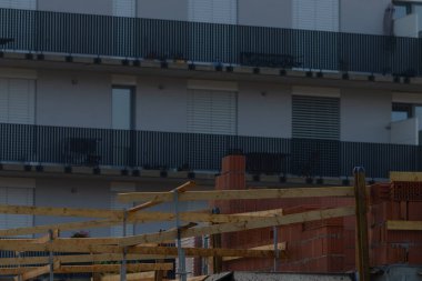 Güvenlik bariyerleri ve mürettebat araçlarıyla balkon onarımı görünür, ahşap parantez ve kıskaçlar koruyucu oluşturur