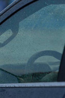 Gösterge panelini çevreleyen yağmur lekeli havan topları, yağmurlu ön cam ve acele etmeyen sürücü duraksaması, yağmurla kaplı araç iç kısımları kasvetli yol kenarı duraklarında sessiz bir anı yakalıyor.