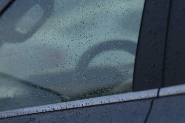 Direksiyon silueti olan ıslak araba penceresi, cama yapışan yağmur damlaları, karamsar, işe gidiş-dönüş yansıması