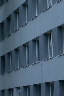 Kurumsal cephe, serin tonlar ve sığ derinlik arasında ritmik desen oluşturan yoğun pencere sırası