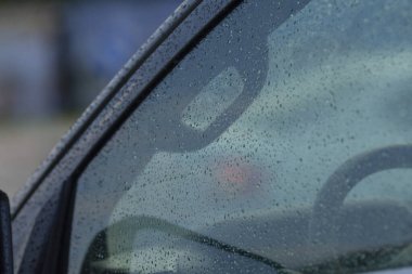 Yağmurlu çizgili ön cam direksiyon, damlacıklı kabin manzarası, bulanık ışıklar, karamsar iç siluet, durağan iç yolculuk ve yansıtıcı atmosfer, banliyö sırasında korunaklı bir an.