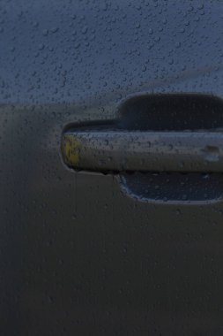 Arabanın kapı kolunda yağmur damlaları var. Şehir ışığını yansıtıyor. Islak dış detay banliyö sakinlerinin geldiğini gösteriyor.
