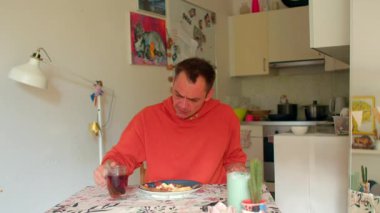 Kahvaltı masasında çay yudumlayan beyaz bir adam, dinlenmek için duraklayan bir emekli, kırmızı kazak, basit mutfak arka planı.,