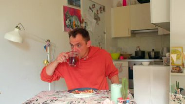 Beyaz adam mutfak masasında kaşıkla içki karıştırıyor. Amatör karışımbilimci evde kokteyl deneyleri yapıyor.