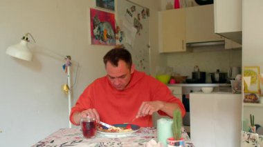 Mutfak masasında yemek kesen beyaz adam, çatal ve bıçakla ev yemeği tatma tabağı, kırmızı kazak, yemek tabağı.