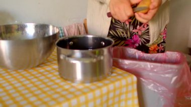 Elma kabuğu soyulmuş, kadın eli yakın çekimde metal tencerenin üzerinde soyucu, gingham masa örtüsü kullanıyor.,