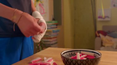 Bandajlı eller, ahşap masa, dikkatli sıralama ve envanter üzerine desenli kaseye çoklu pembe eşyalar yerleştiriyor.,