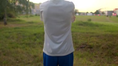 Geniş çekim Kafkas ergen bakış açısı açık alanda kollarını ve omuzlarını esneterek, sıcak günbatımının ışıltısı,