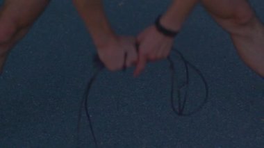 Antrenör elleri ayaklara yakın atlama halatı ve asfalt üzerinde spor ayakkabıları bağlıyor.