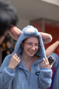 Yakın çekim katılımcısı mavi tavşan başlığını ayarlıyor, kameraya hafifçe ışıldıyor, sokak arkası bulanık, renkli kalabalık, neşeli jest, CZ yakalayan gözlük, Prag, Na prikope, 2.8.25