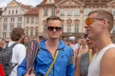 Prag Meydanı 'ndaki mavi ceketli adam gökkuşağı aksesuar festivali atmosferi taşıyan kalabalık ve barok binalarla çevrili gülümseyen yüzler CZ, Prag, Na prikope, 2.8.25