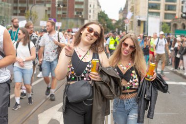 İçki ve güneş gözlükleriyle gülümseyen iki kadın, günlük ikili yürüyüş gururu, eşleşen boncuklar, tezahürat kutuları, gevşetilmiş sokak havası CZ, Prag, Na prikope, 2.8.25