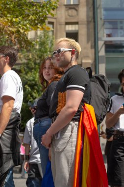 Pelerin olarak gökkuşağı bayrağı takan çift geçit törenini izliyor, şefkat dolu kucaklaşma ve dayanışma görünüyor, CZ, Prag, Na prikope, 2.8.25 'te ortaklık ve paylaşılan gurur