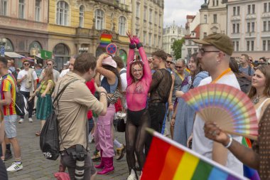 Fotoğrafçı, kamera, odaklanmış duruş, basın rozeti ve görünür teçhizat ile dans eden kalabalığı yakalıyor. Enerjik sahne, yerde sunum tarzı CZ, Prag, Na prikope, 2.8.25