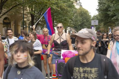 Bayraklar ve cesur kostümlerle yürüyen çeşitli gruplar, koşum takımı ve güneş gözlükleriyle festivale katılan enerjik kalabalık, renkli kıyafetler ve kendinden emin CZ, Prag, Na prikope, 2.8.25