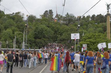 Prag köprüsünde yürüyen kalabalık, gökkuşağı bayrakları ve afişler, eşitlik ve hakları kutlayan binlerce insan, renkli kıyafetler, tramvay CZ, Prag, Na prikope, 2.8.25