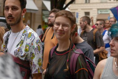 Prag kalabalığında odaklanmış bir yürüyüşçü, gözlüklü ve sırt çantalı gönüllü bir öğrenci, özenli ifade, yakınlardaki çeşitli insanlar, renkli üstler ve bayraklar, CZ, Prag, Na prikope, 2.8.25