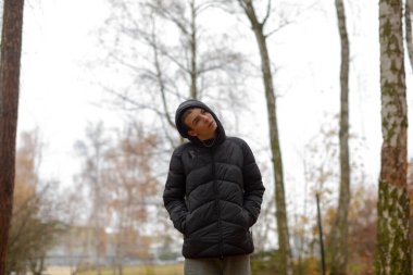 Parkta bereli ve kabarık ceketli, elleri ceplerinde, dalgın dalgın dalgın dalgın dalgın dalları, huş gövdeleri ve uzak konutlar, sessiz ekolojik gözlem,