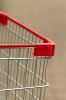 Sıcak gün ışığı, alışveriş arabasının detaylarını aydınlatır, alışveriş ikonu görüntüleriyle eşleştirilmiş minimalist doku, yumuşak bulanık şehir arka planına karşı kırmızı alışveriş sepetinin yakın plan görüntüsü