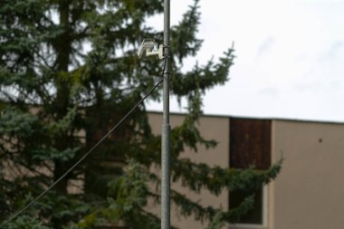 Uzun ladin, açılı armatür ve kapalı bej bina, üstten kablolar ve kapalı gün ışığı, fonksiyonel geometri ile kentsel kenar ruh hali, belediye kurulum ve bakım bağlam yanında metal lamba