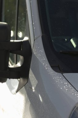 Parlak yansıtıcı yüzeylere sahip yağmurlu araçlar su damlacıklarını ve yansımalarını yakalıyor, kentsel dağıtım kamyonları parlak yüzeylerinde su damlacıkları ile parıldayan ıslak yansımalar sergiliyor