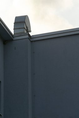 Yumuşak gökyüzü olan köşedeki çatı menfezi. Açılı çatı köşesi, havalandırma borusu ve baş etme, sessiz alacakaranlık tonları, şehir silueti ve sessiz sanayi kenarı gösteriyor..