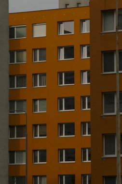 Pencere ızgaralı turuncu bina, şehir planlayıcısı hizalama ve ritmi denetliyor, düz yükseklik ve düzgün dış görünüş, geometriyi vurgulayan nötr gökyüzü arka planı