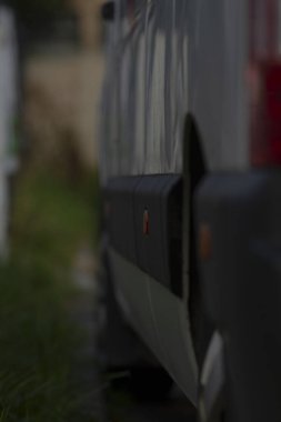 loş ışıklı minibüs yan yansıması, parlak boyalı düşük ışık atmosferi ve ince röfleler, gece vardiyası bakım titreşimi gece vardiyası valesi veya kurye molası, derin gölgeler ve sinematik atmosfer