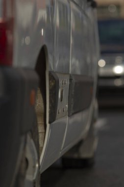 Teslimat minibüsü bekliyor, paketler görünür bir şekilde park edilmiş, şehir çevresi hareketli, beyaz kurye minibüsü parselli ve şehir aydınlatmalı caddelerde duruyor.