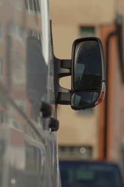 Van kenarı aynası şehir caddesini yansıtıyor ve sığ derinlikte cepheler inşa ediyor, trafiği ve ılık tonları bulanıklaştırıyor, perspektif, güvenlik ve şehir içi ulaşım bağlamını vurguluyor