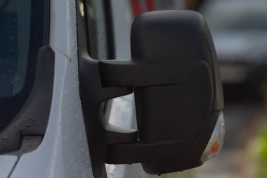 Yakın plan siyah minibüs yan aynası, görünürlük ve gösterge, bütünleşik sinyalli desenli plastik konut, sığ derinlik alanı ve bulanık sokak arka planı, ticari yol içeriği