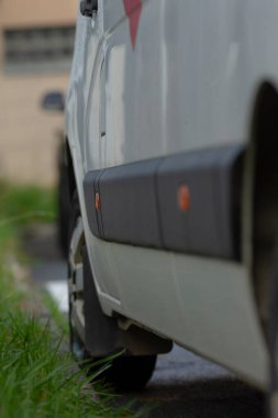 ıslak kamyonet yan ve tekerlek ayrıntıları, su damlacıkları aşağı panelde ve çimenlerin yanında lastik, durulama izleri gösteren yol kenarı görüntüsü, boyalı yüzeyde ince yansımalar, teslimat vardiyası hazırlıkları,