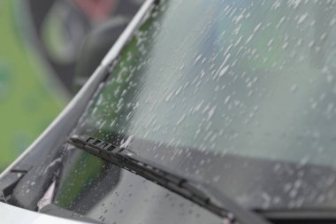 Silecek temizleme görüntüsü, sileceklerin temizlenmesi, sileceklerin hareket halinde olduğu canlı şehir manzarası, kentsel çevrede yakalanan eğimli cam yüzeyde dinamik su izleri.