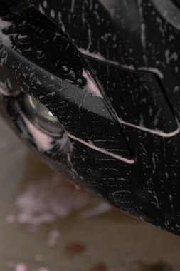 Siyah tampon hafif durulamayla temizlenmiş, şehir gezici temizleyici ışıl ışıl ışıl parlıyor, araba tamponu kapanışı temiz sabun izleri ve şehir ortamında parlak bir yüzey ile tamamlanıyor.